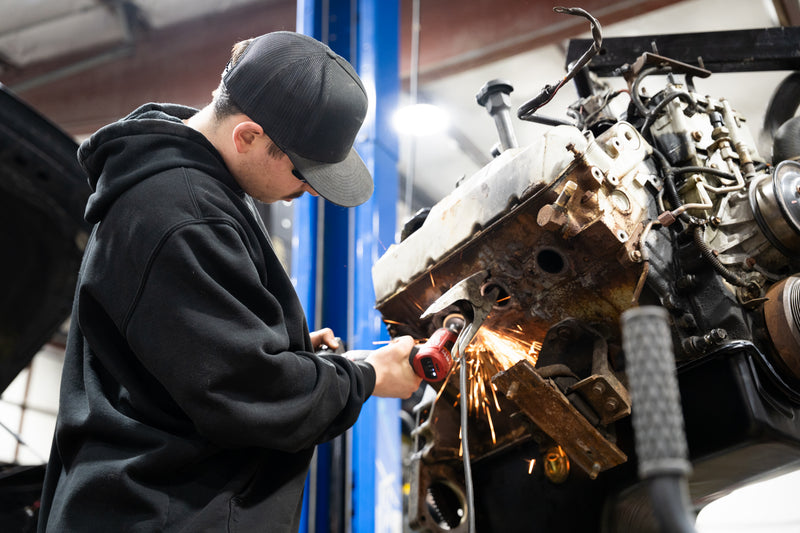 Person working on a car engine with tools in a garage setting